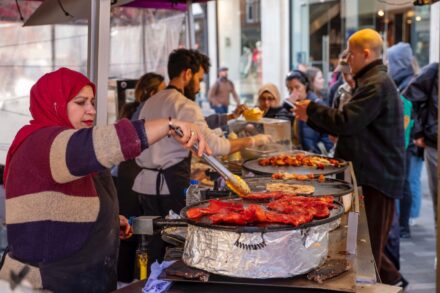 Seasoned chicken on large circle grill being cooked by man in a branded apron.
