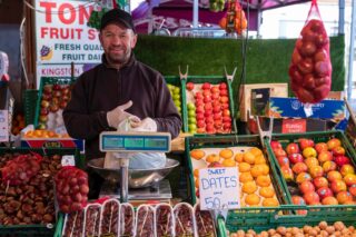 A range of fresh fruit and veg with man bending over to pick something up.