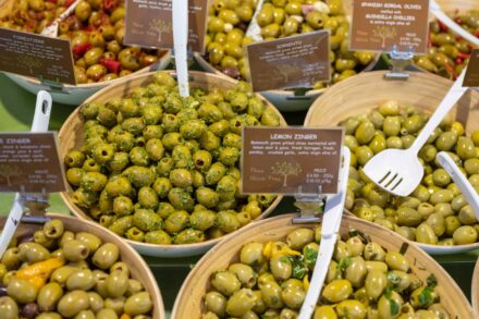 Pots of olives on stall counter with labels on each wooden pot. With dried chillies hanging on the left hand side.