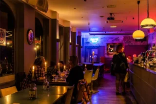 People sitting in lowly lit bar with neon light at far end of room